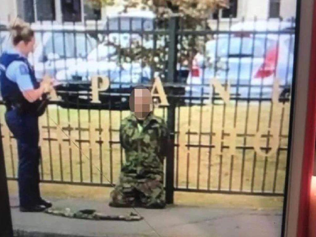 New Zealand Police arrest one individual in camo uniform in front of Papanui High School. In front of him there is something that looks like wrapped rifle.   